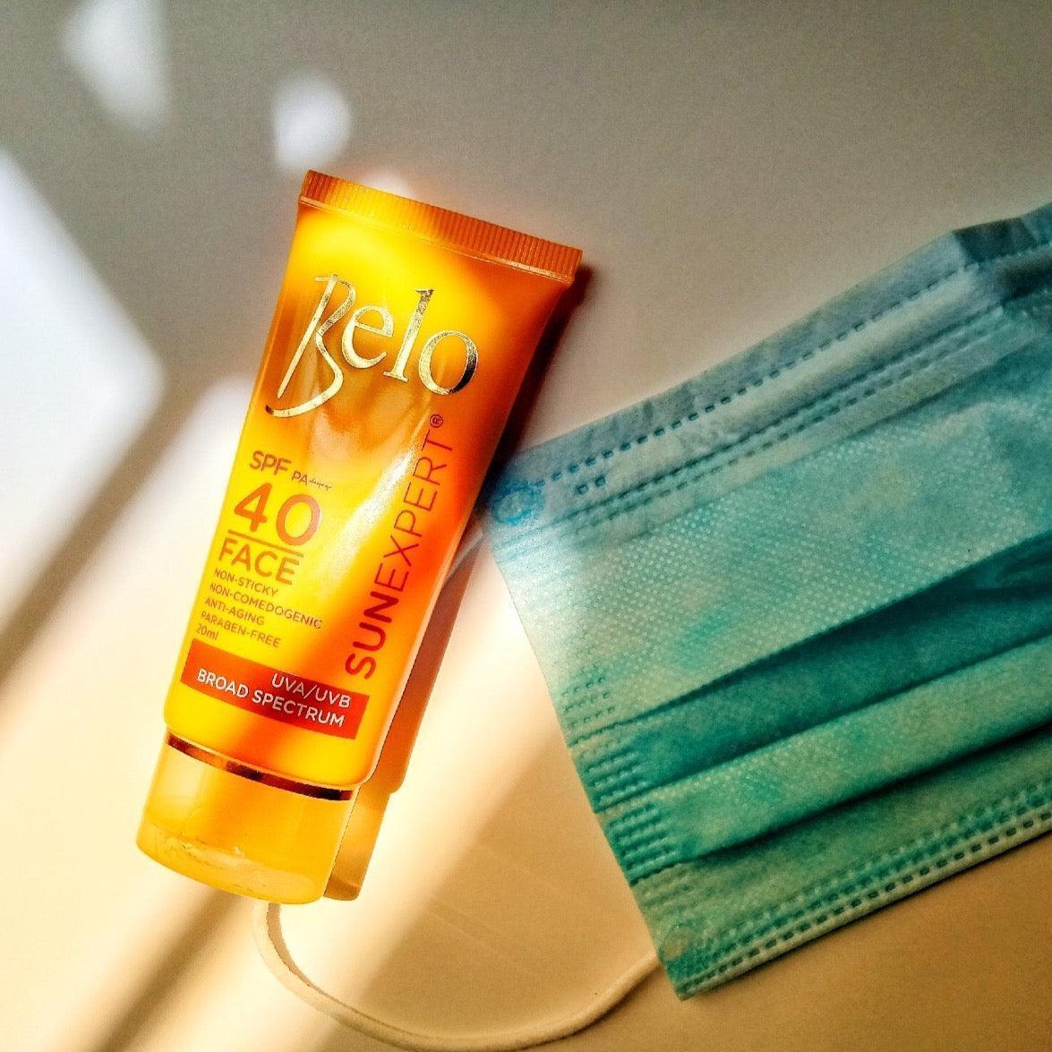 Belo SunExpert Face Cover SPF 40 sunscreen tube beside a blue disposable face mask on a light surface