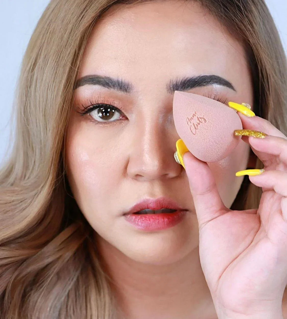 Woman holding a pink makeup sponge with script logo, closeup of face and beauty tool