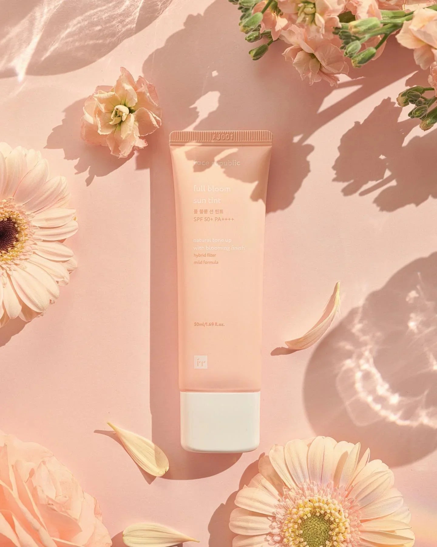 Full Bloom Sun Tint SPF 50+ tube with flowers on pink background, skincare product flatlay