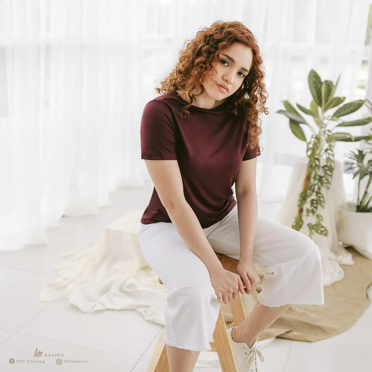 Woman in a maroon slim fit t-shirt and white cropped pants sitting indoors, casual style