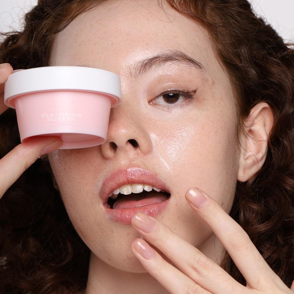Woman holding pink cleansing butter jar near face with dewy, glowing skin