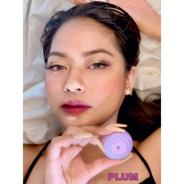 Woman with plum-toned lips holding purple lip balm container labeled Plum