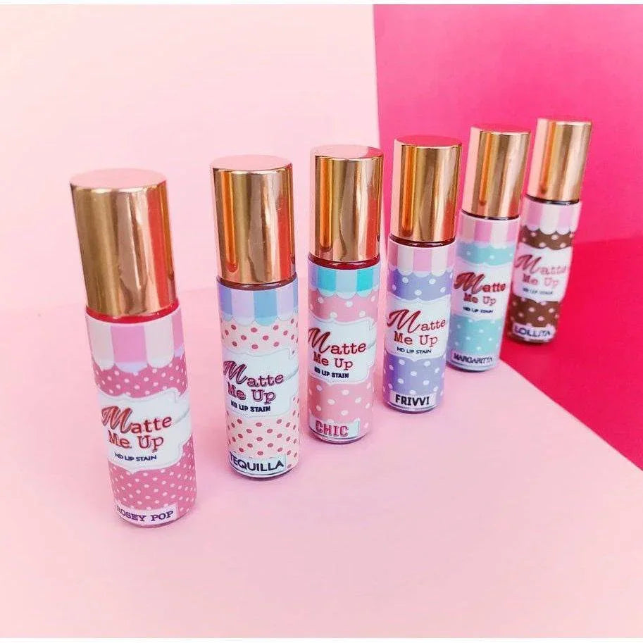 Six Matte Me Up lip stain tubes in pastel packaging on a pink background