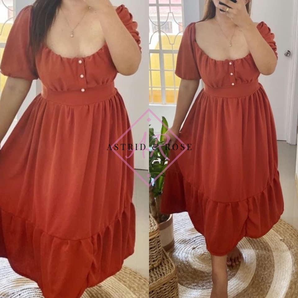 Plus size Inah dress in rust red with puff sleeves and button detail, displayed indoors.