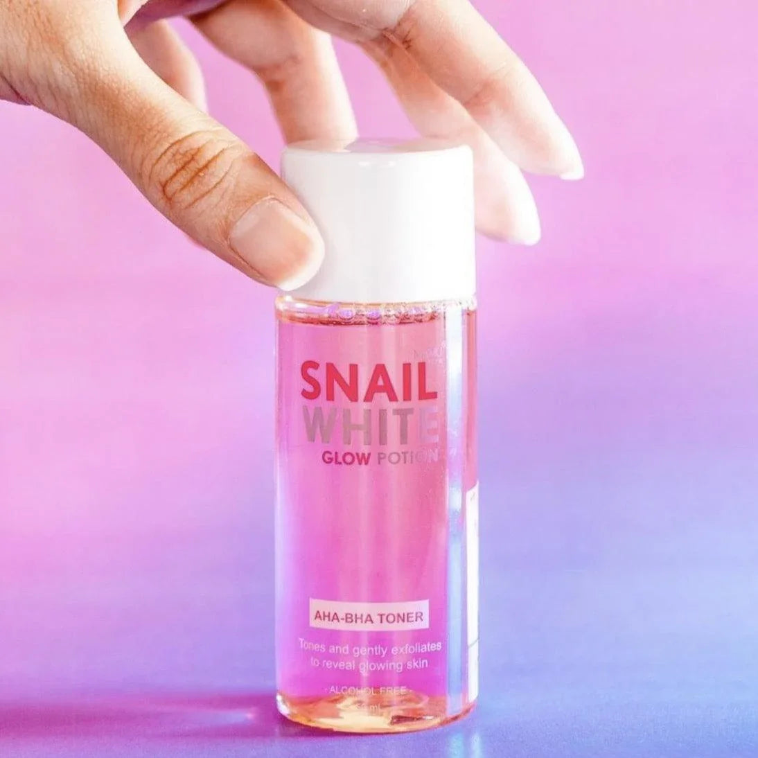 Hand holding Snail White Glow Potion AHA-BHA toner bottle on a pink gradient background
