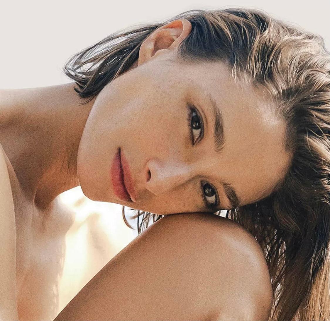 Close-up of woman with natural makeup and glowing skin, resting her head on her knee