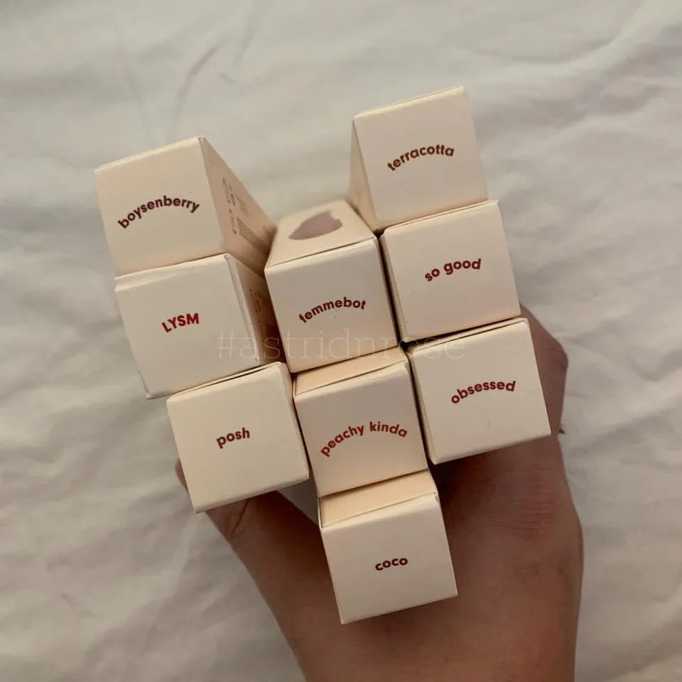 Hand holding assorted lip product boxes in shades boysenberry, terracotta, peachy, and coco