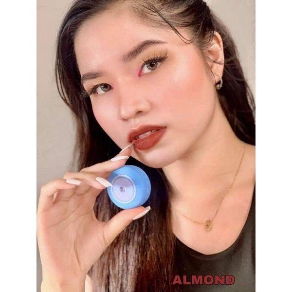 Woman with glossy almond-colored lips holding blue lip balm container, natural makeup look